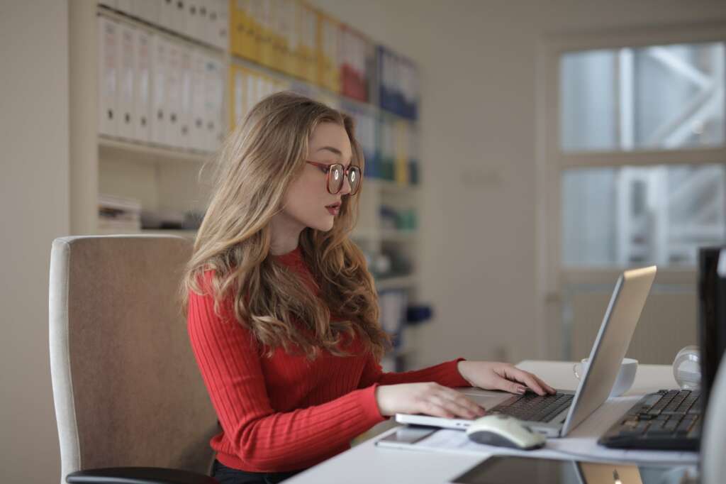 woman in red long sleeve shirt wearing eyeglasses using a laptop