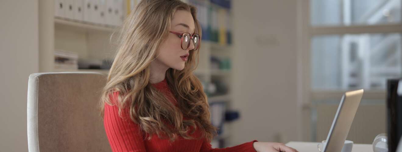woman in red long sleeve shirt wearing eyeglasses using a laptop