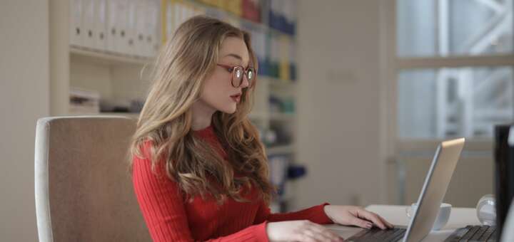 woman in red long sleeve shirt wearing eyeglasses using a laptop